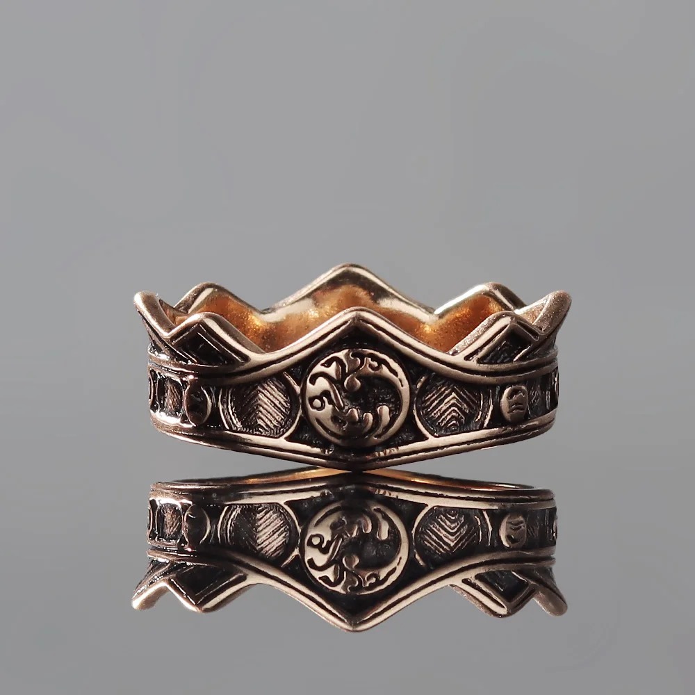 Anel coroa Targaryen bronze/dourado com o brasão do dragão, de Game of Thrones, sobre fundo cinza