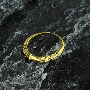 Anel dourado aberto, de metal com relevo envelhecido, inspirado em Elden Ring, sobre pedra escura