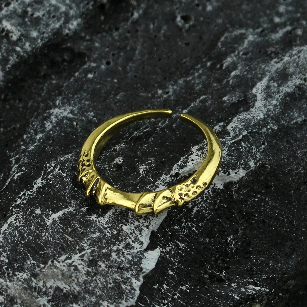 Anel dourado aberto, de metal com relevo envelhecido, inspirado em Elden Ring, sobre pedra escura
