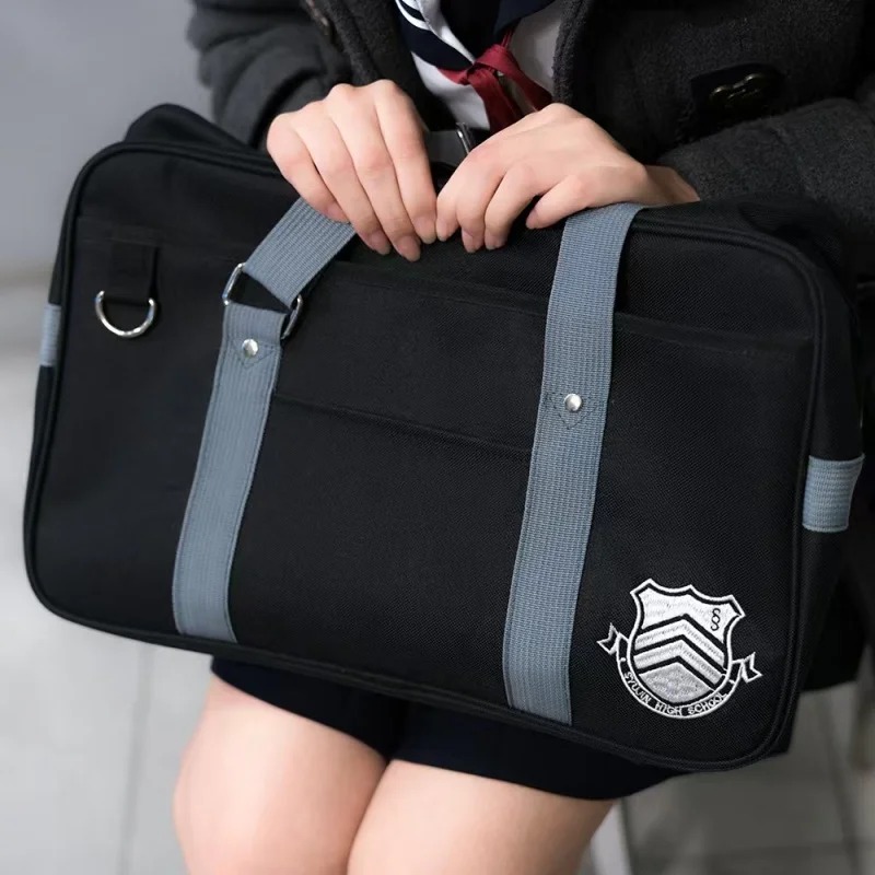 Bolsa da Shujin, Persona 5, erguida pelas alças cinza com o brasão bordado em evidência