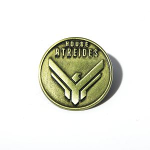 Broche redondo de metal bronze com o brasão da Casa Atreides, de Duna, sobre fundo branco