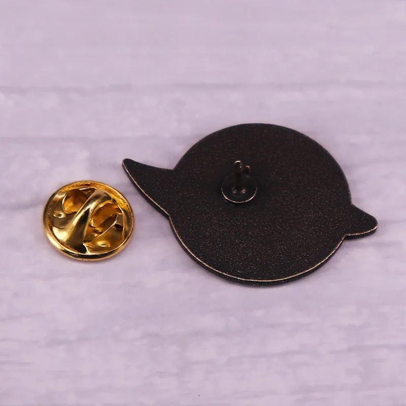 Parte de trás do broche de Steins;Gate, com o pino e o fecho de borboleta dourado ao lado