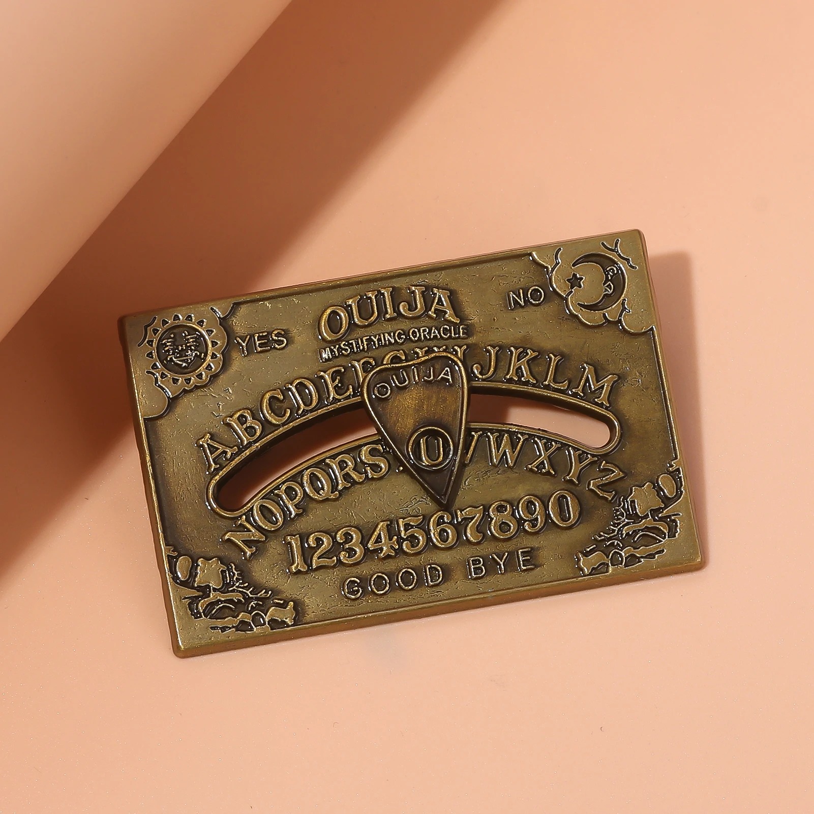 Broche do tabuleiro Ouija em bronze, com sol e lua nos cantos, sobre fundo laranja e rosa
