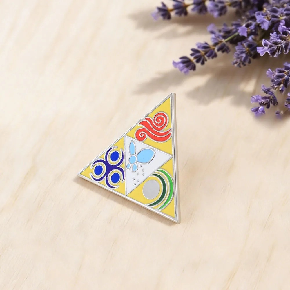 Broche Triforce de Zelda sobre mesa de madeira clara, ao lado de flores de lavanda