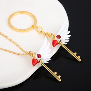 Chaveiro e colar da chave dourada com asas brancas e cristal vermelho, sobre fundo preto e branco
