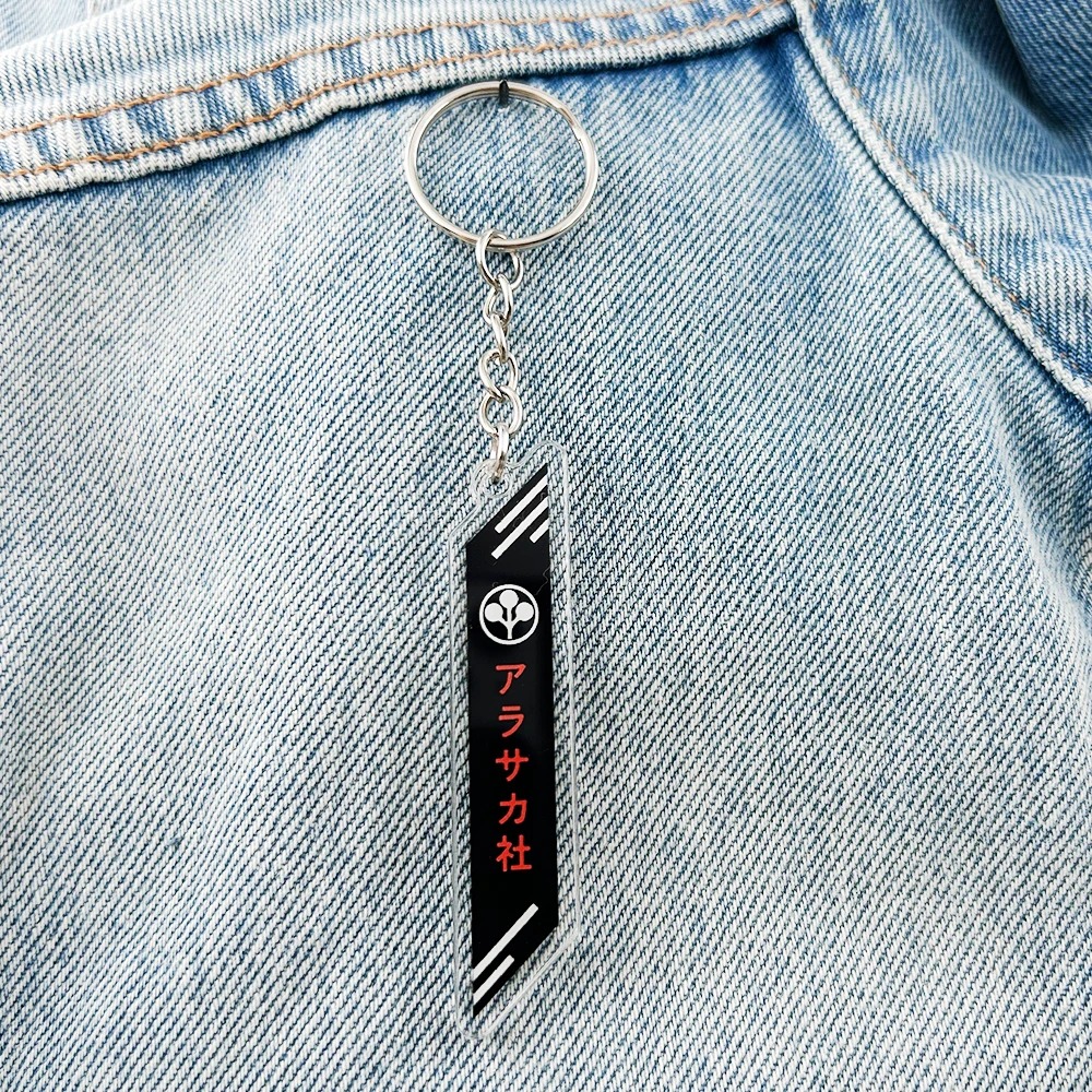 Chaveiro do logo da Arasaka preso a um tecido jeans azul