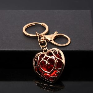 Chaveiro do Coração Container vermelho em metal dourado, com argola e mosquetão, sobre superfície preta