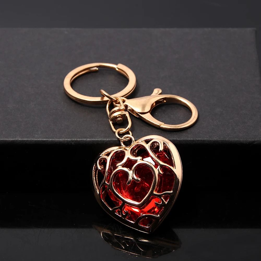 Chaveiro do Coração Container vermelho em metal dourado, com argola e mosquetão, sobre superfície preta
