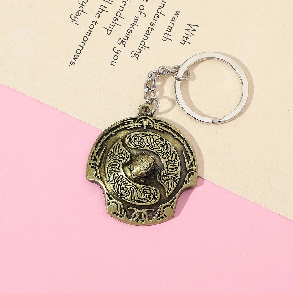 Chaveiro do escudo Aegis dos Campeões, de Dota 2, sobre fundo rosa e papel de partitura