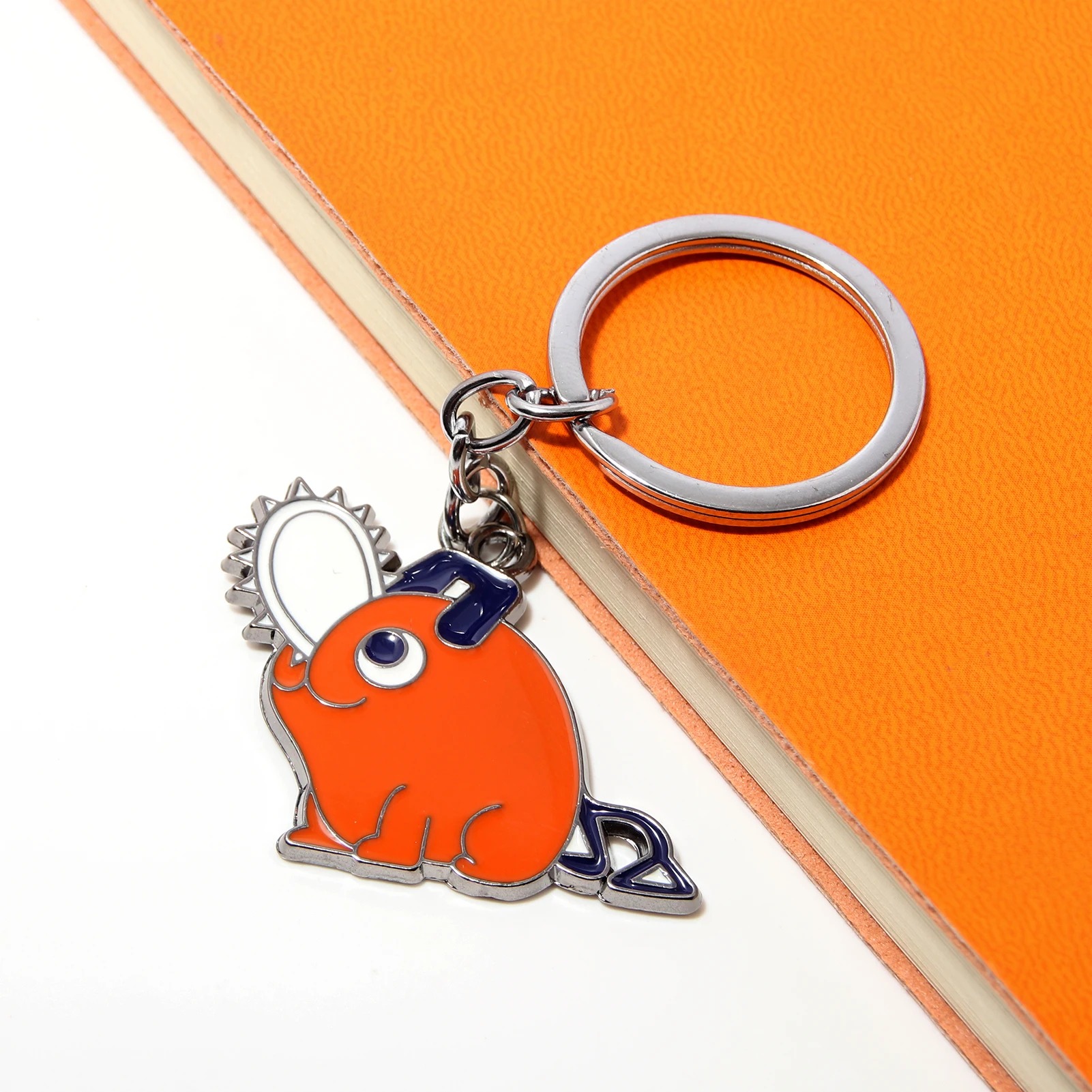 Chaveiro laranja do Pochita em metal esmaltado sobre papel laranja