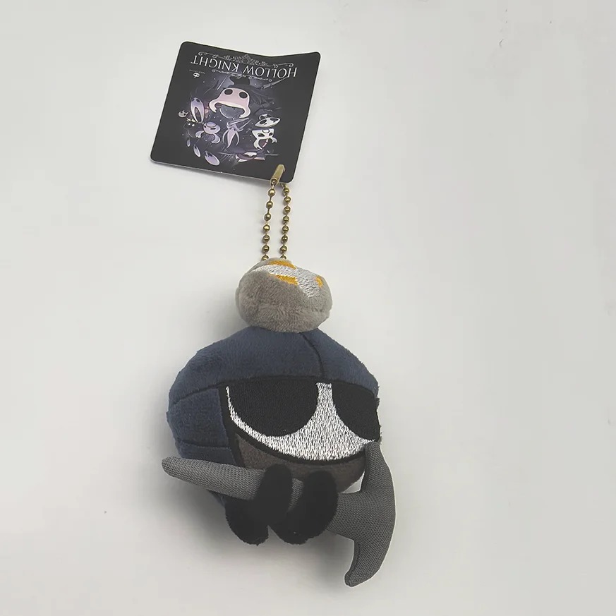 Zote de Hollow Knight em pelúcia mini, com capacete azul e capa cinza, preso numa corrente de bolinhas