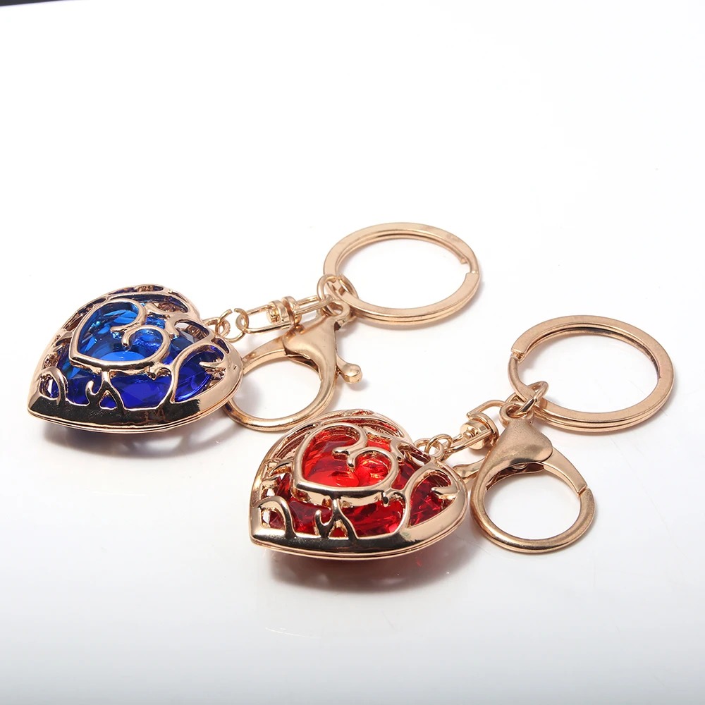 Dois chaveiros de coração dourado de Zelda, com pedras azul e vermelha e argolas douradas