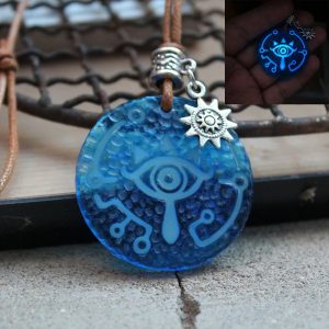 Olho Sheikah de Zelda em chaveiro verde-água sobre madeira, com argola e sol prateado