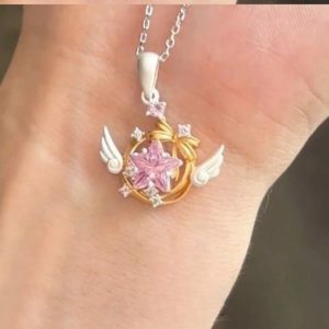 Colar de estrela rosa com asas brancas, de Cardcaptor Sakura, apoiado na palma de uma mão