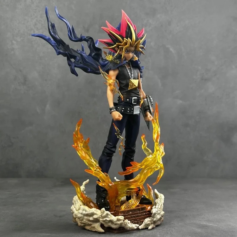 Estátua do Yugi Muto de lado, com capa azul esvoaçante e chamas amarelas na base