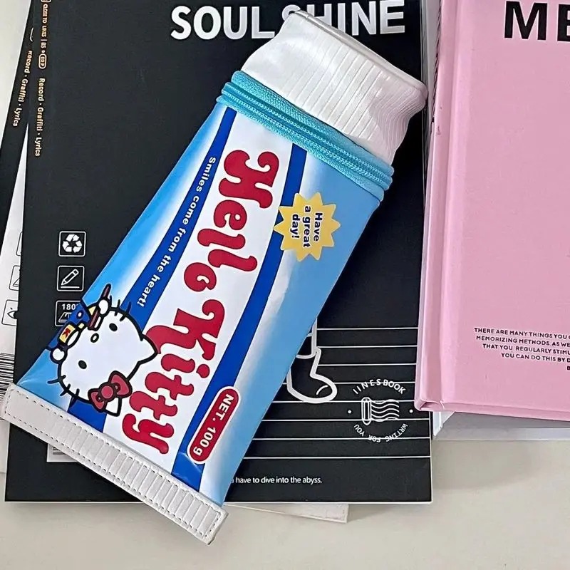 Estojo azul da Hello Kitty em formato de tubo, com mini figura rosa na tampa, sobre cadernos