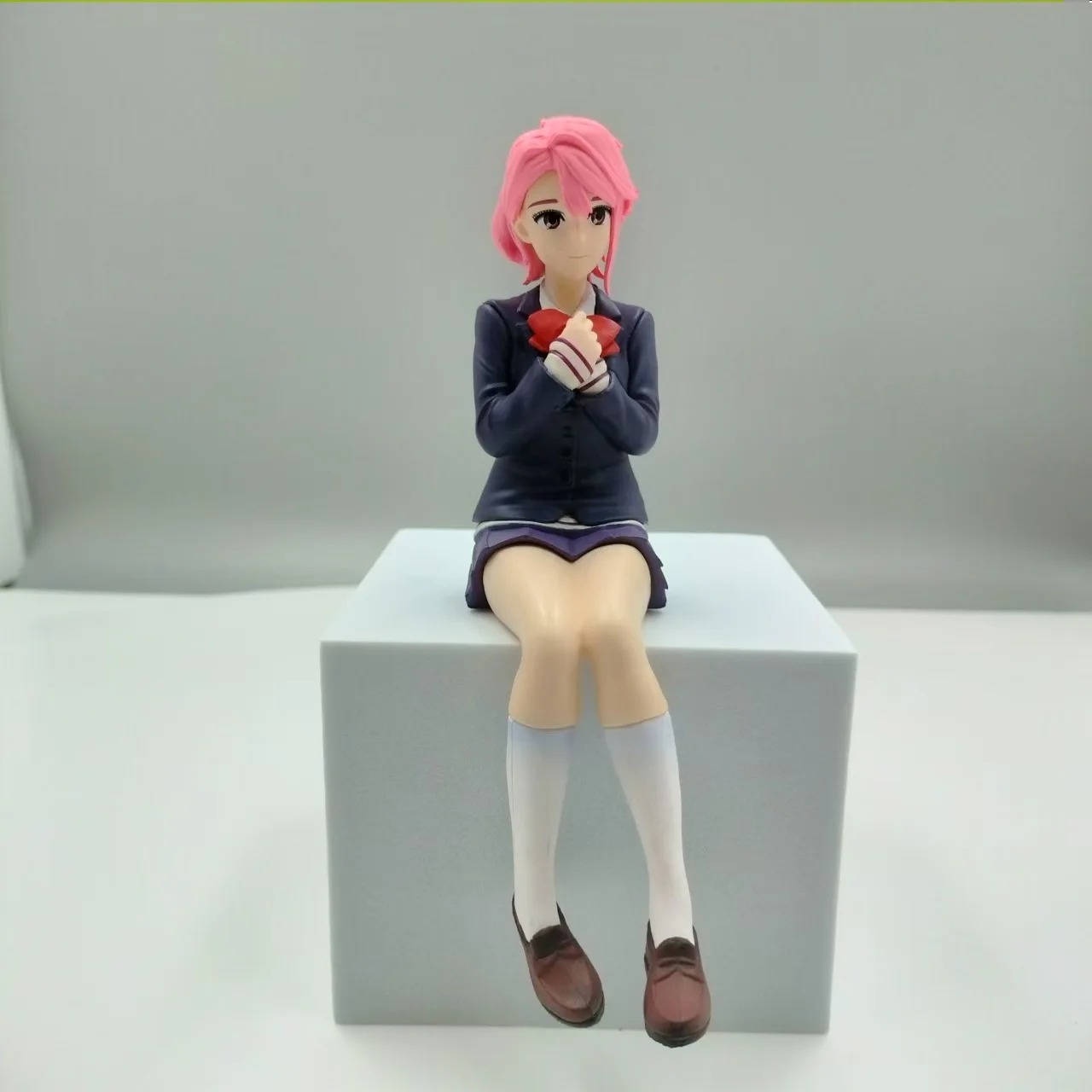 Aira Shiratori, de Dandadan, em figure sentada de uniforme escolar azul sobre um bloco branco