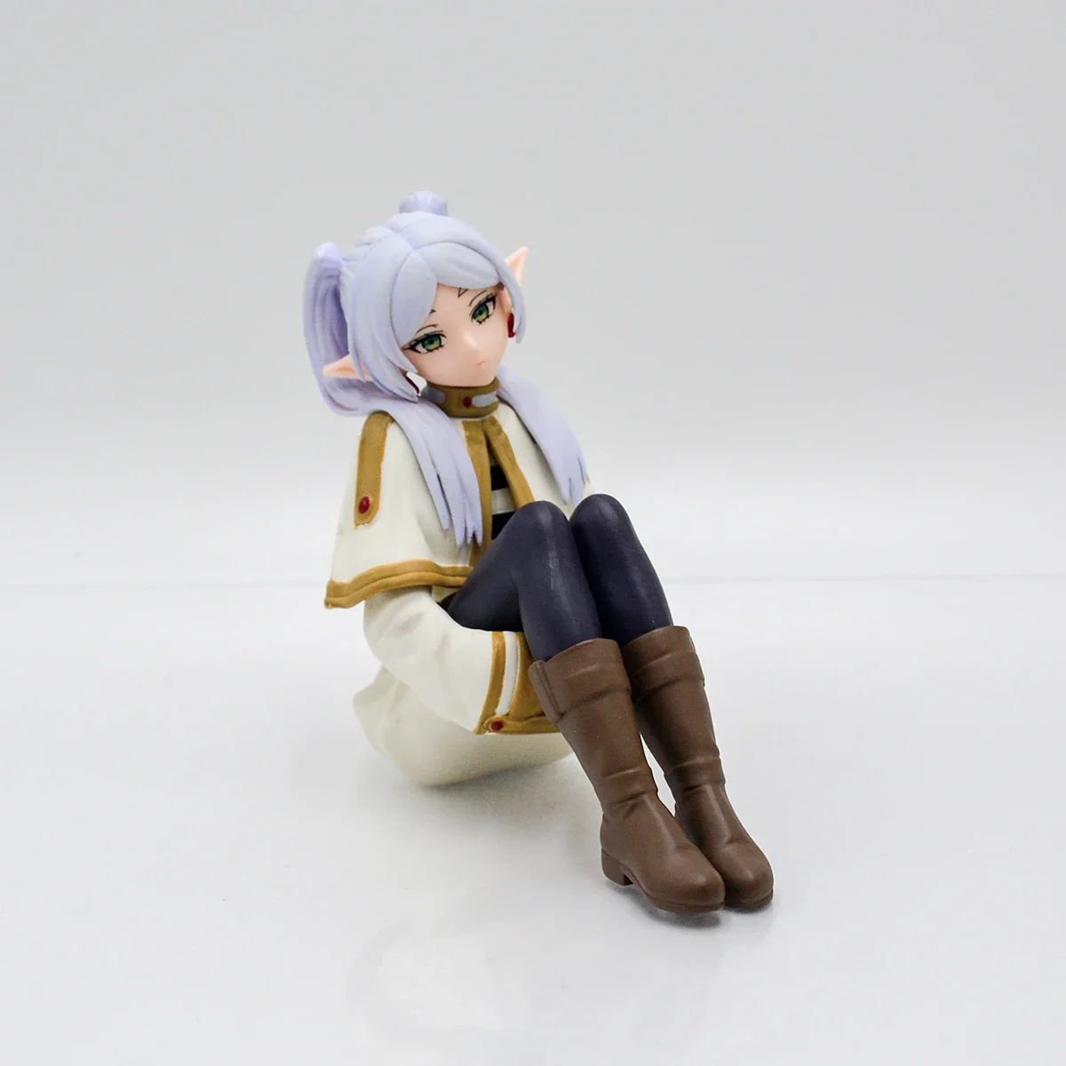 Figure sentada da Frieren, de Frieren e a Jornada para o Além, com capa branca e botas