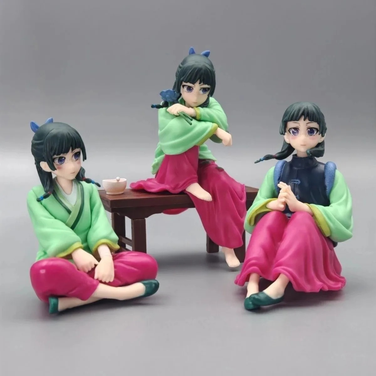 Três figures da Maomao, de Diários de uma Apotecária, sentadas em poses distintas, uma delas no banco