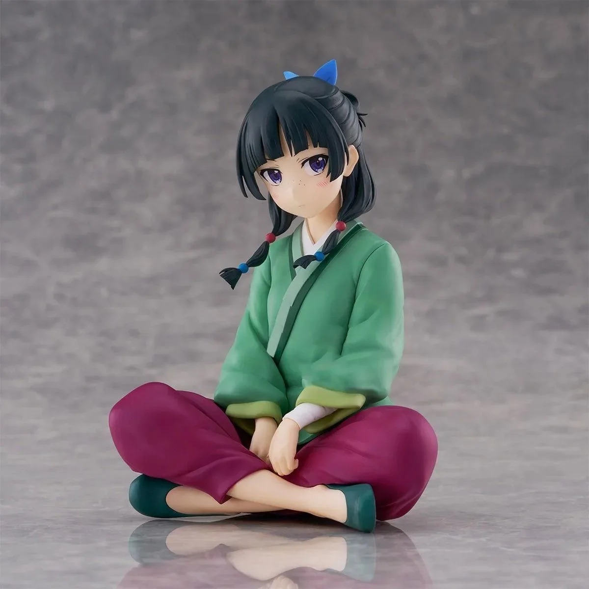 Figure da Maomao, de Diários de uma Apotecária, de pernas cruzadas, com roupa verde e calça rosa