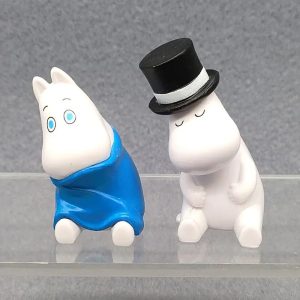 Figure branca do Moomin com capa azul ao lado do pai Moomin, de cartola preta, em PVC