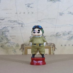 Porco Rosso de uniforme verde-oliva, capacete e óculos sobre base vermelha