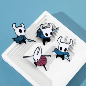 Quatro broches esmaltados de Hollow Knight, com o Cavaleiro e a Hornet, sobre fundo azul