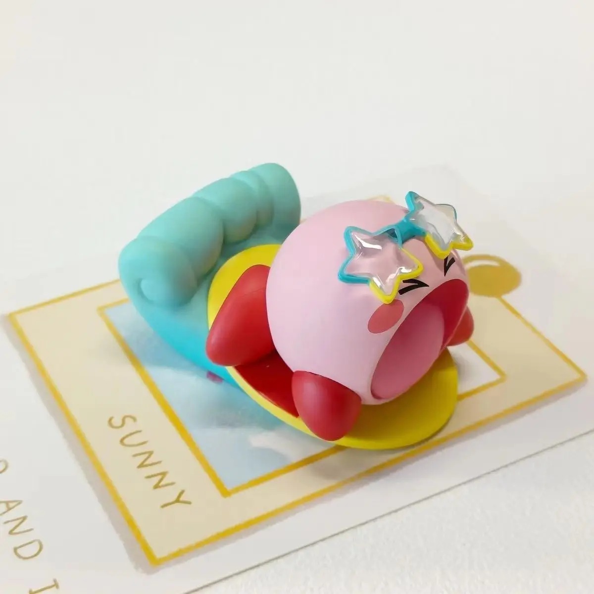 Kirby deitado numa boia azul, de estrelas nos olhos, na série praia