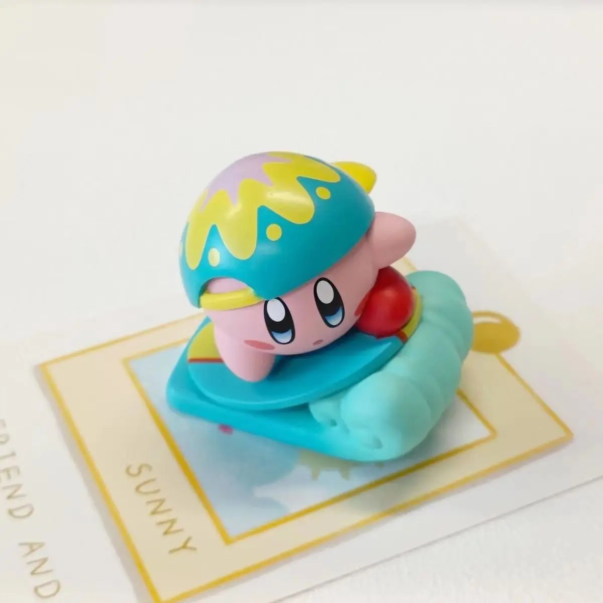 Kirby de touca amarela e azul sobre uma prancha azul
