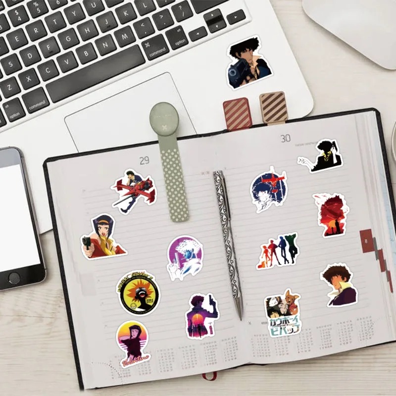 Adesivos de Cowboy Bebop colados num caderno, ao lado de um notebook
