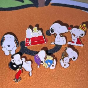 Kit de sete pins esmaltados do Snoopy em poses diferentes, sobre fundo laranja