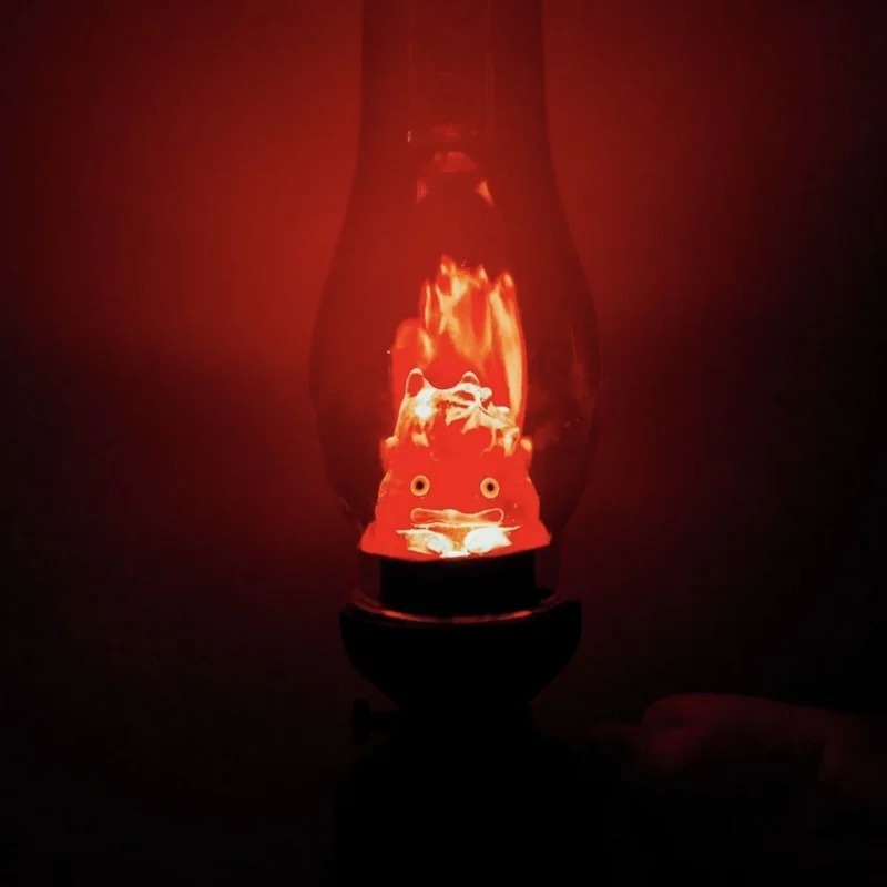 Calcifer brilhando em laranja na penumbra, dentro da luminária de lampião