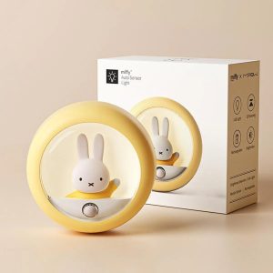 Luminária amarela e redonda com a coelhinha Miffy, ao lado da caixa de embalagem