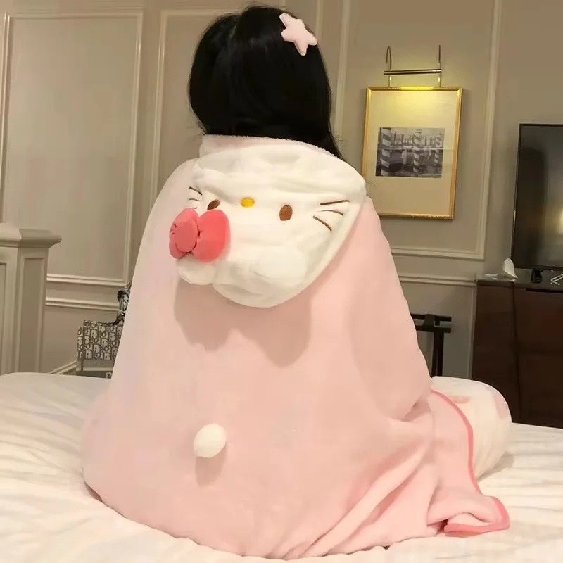Pessoa de costas com a manta rosa de capuz da Hello Kitty, laço rosa e pompom, sentada numa cama
