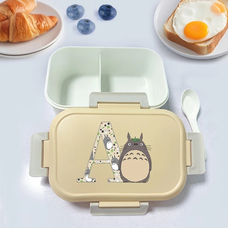 Marmita bento bege do Totoro com a letra A na tampa, junto de pão e ovo