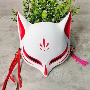 Máscara kitsune branca e vermelha de meia face, com borlas e sininho, sobre fundo de plantas