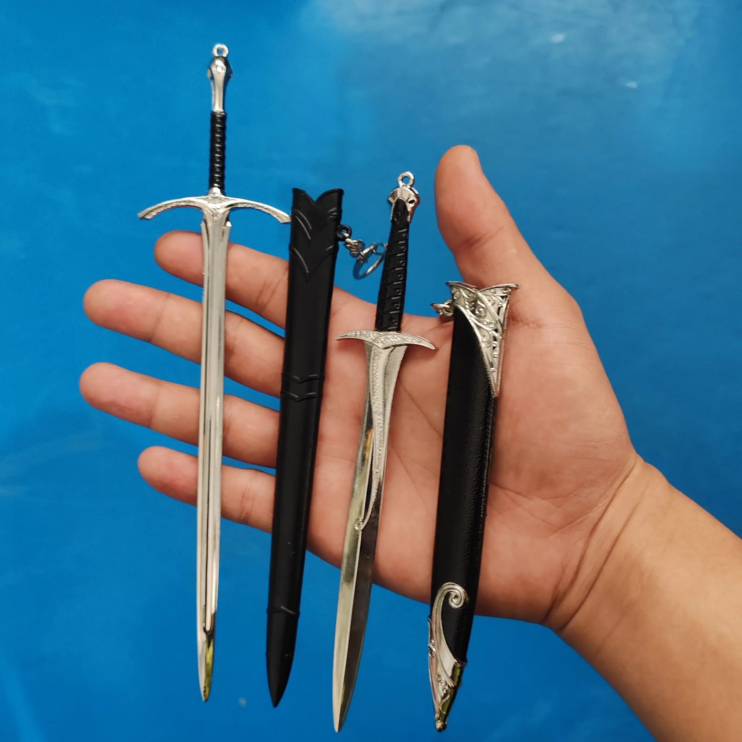 Miniaturas de espadas da Terra-média, com bainhas pretas, seguradas em uma mão