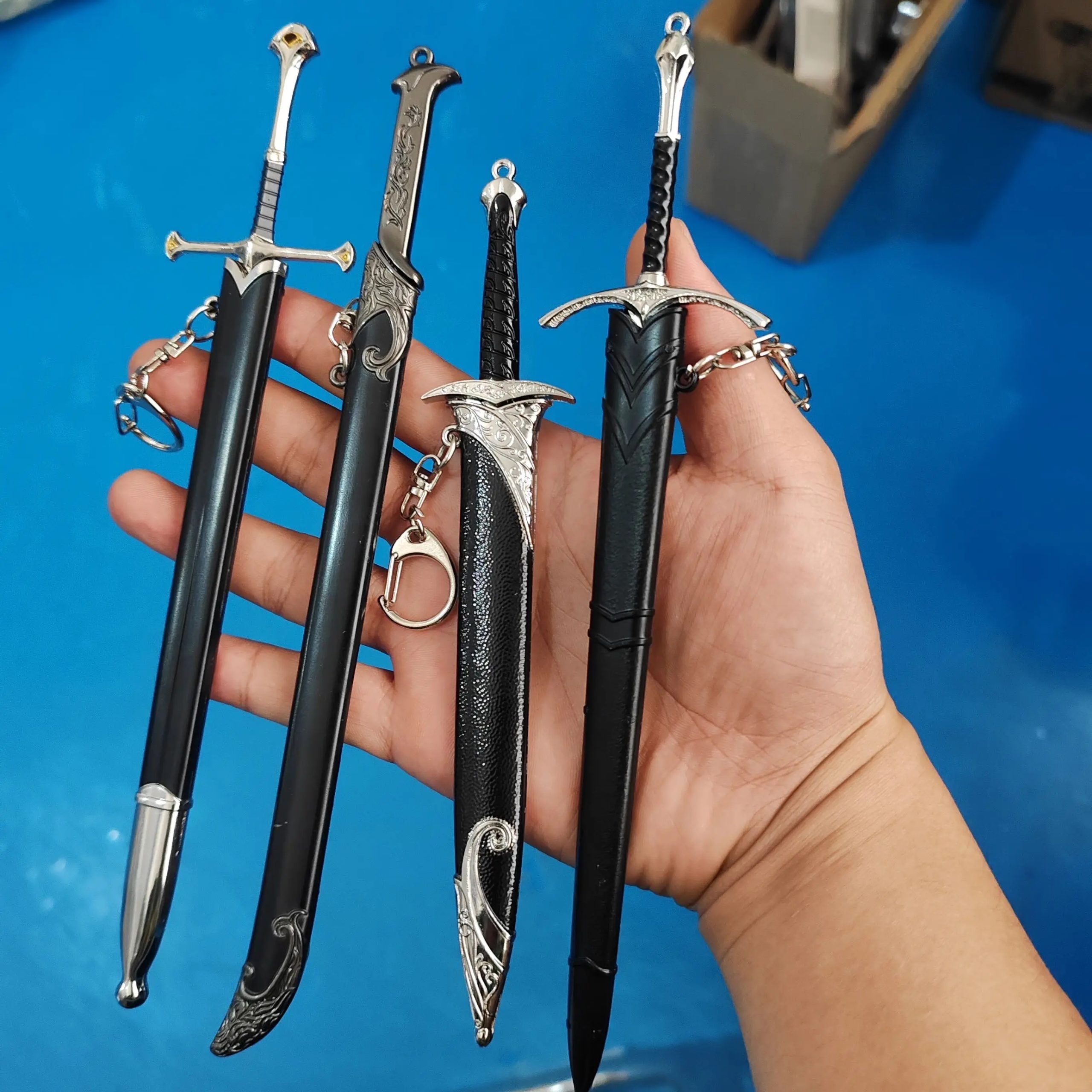 Quatro miniaturas de espadas élficas ao lado de uma mão, mostrando o tamanho de 22 cm