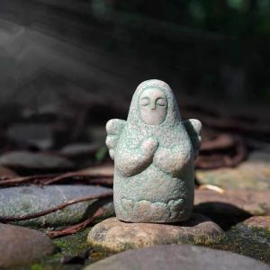 Estatueta da deusa de Breath of the Wild entre pedras no jardim, com mãos em prece e asas