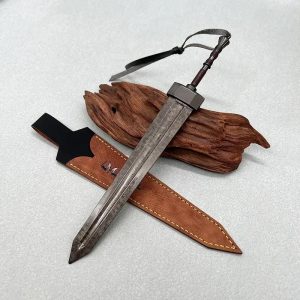 Miniatura da Greatsword de Elden Ring em metal, ao lado da bainha, sobre uma peça de madeira