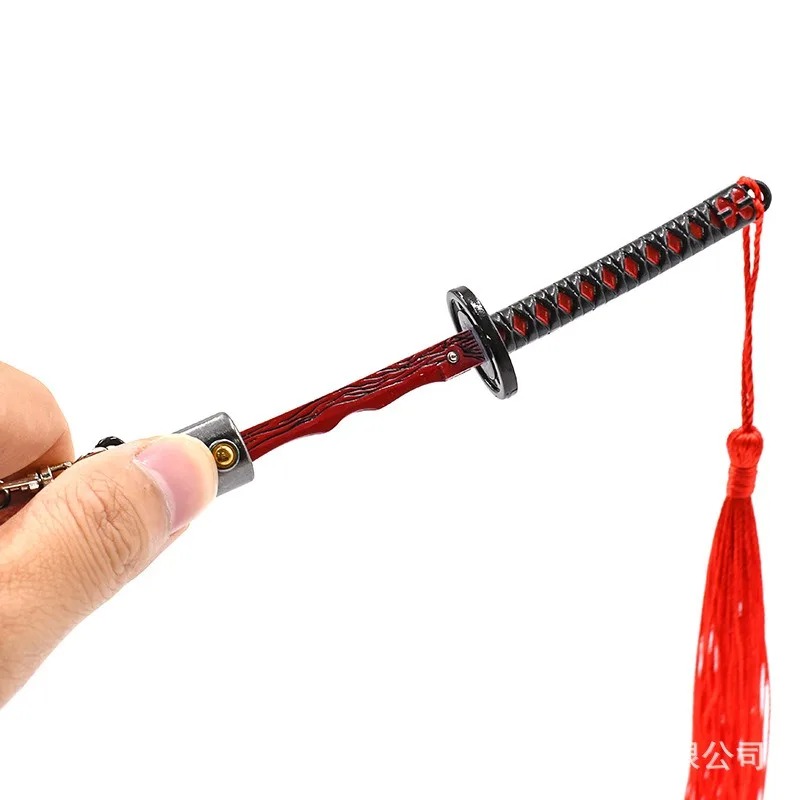 Mão segurando o cabo da katana em miniatura, com fita vermelha