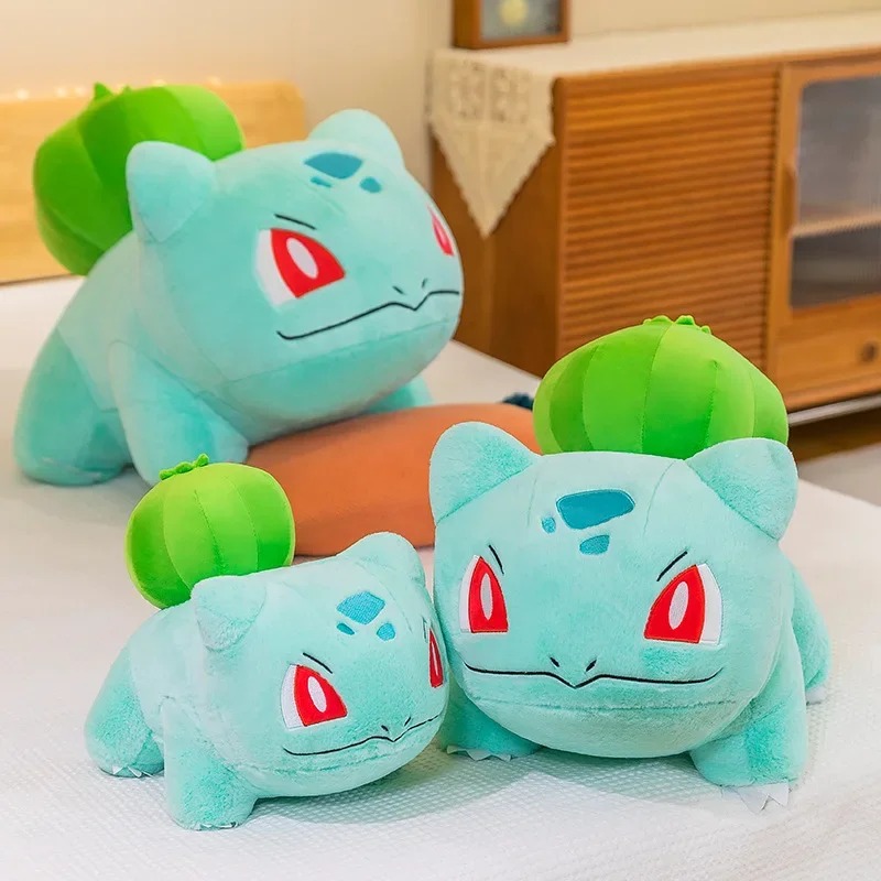 Três pelúcias do Bulbasaur de tamanhos diferentes numa cama