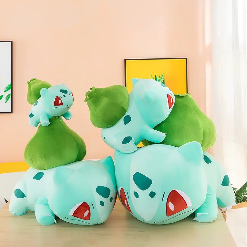 Quatro pelúcias do Bulbasaur lado a lado numa mesa, cada uma de um tamanho