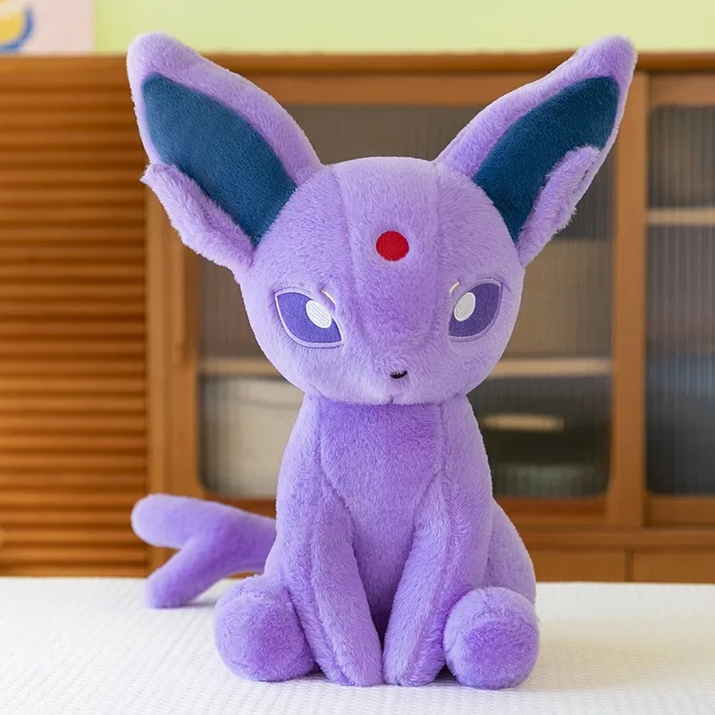 Espeon de pelúcia, de Pokémon, lilás, sentado sobre uma mesa, em foto de produto