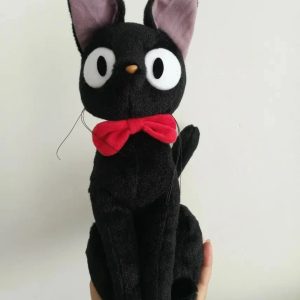 Pelúcia do gato preto Jiji, de O Serviço de Entregas da Kiki, sentada, com olhos grandes e laço vermelho