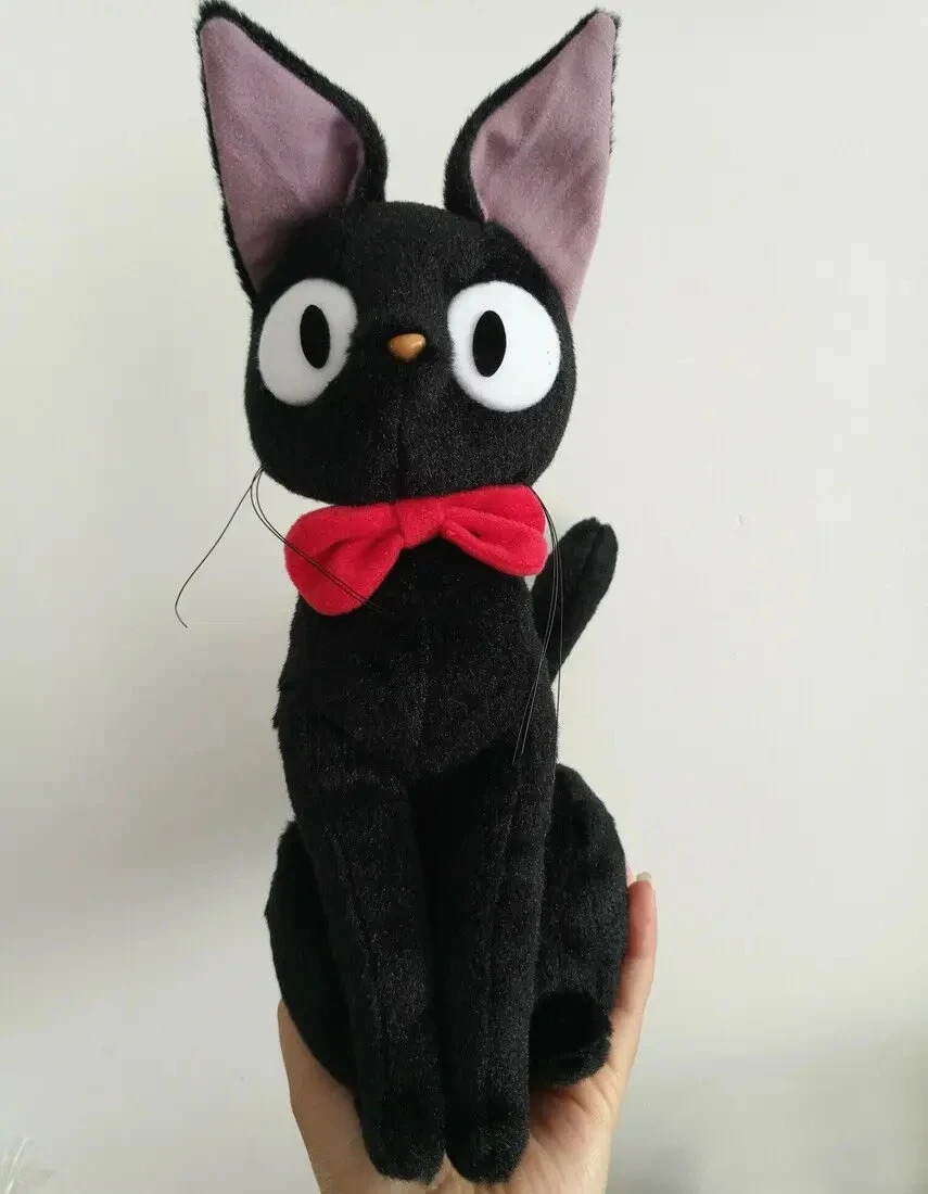 Pelúcia do gato preto Jiji, de O Serviço de Entregas da Kiki, sentada, com olhos grandes e laço vermelho