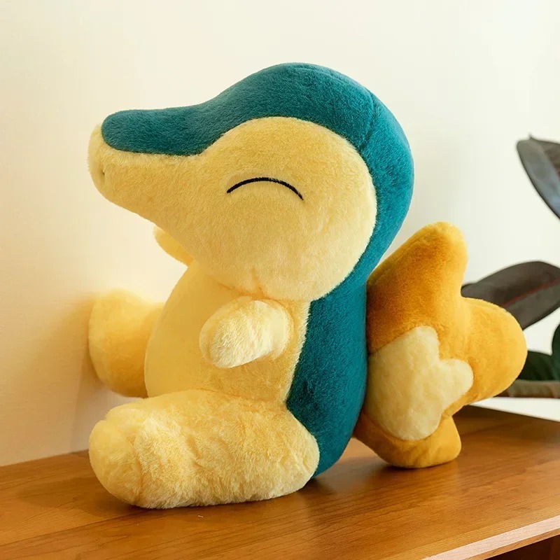 Pelúcia do Cyndaquil de perfil, com dorso azul-petróleo, numa estante