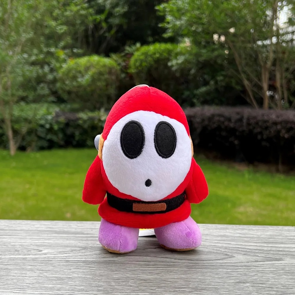 Shy Guy vermelho de Super Mario em pelúcia, sobre uma mureta, com máscara branca bordada