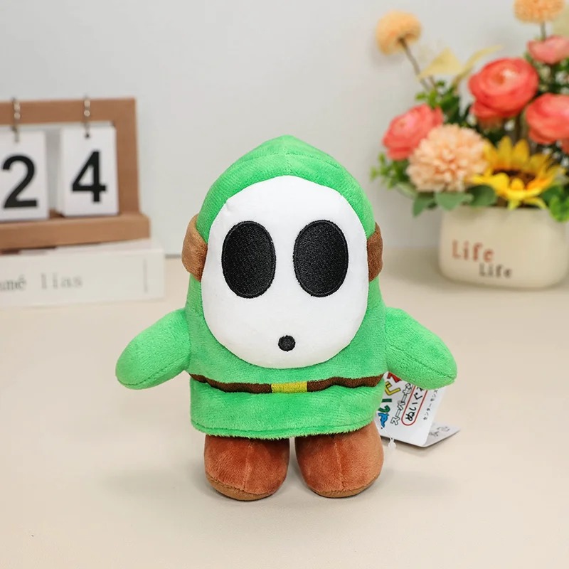 Shy Guy verde de Super Mario em pelúcia, com máscara branca e pés marrons