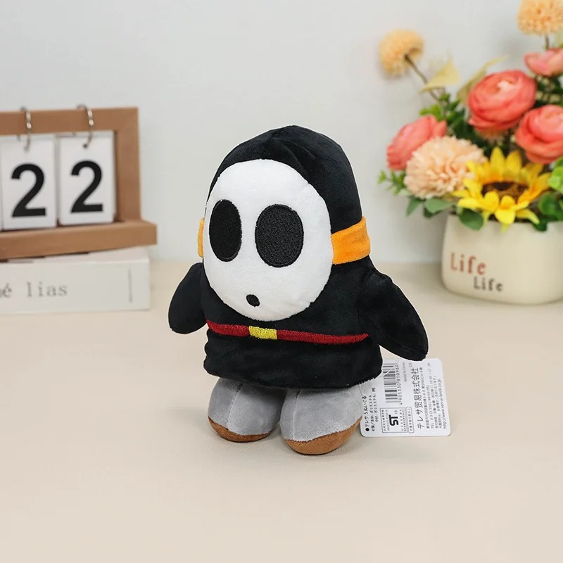 Shy Guy preto de Super Mario em pelúcia, com pés cinza e faixa laranja